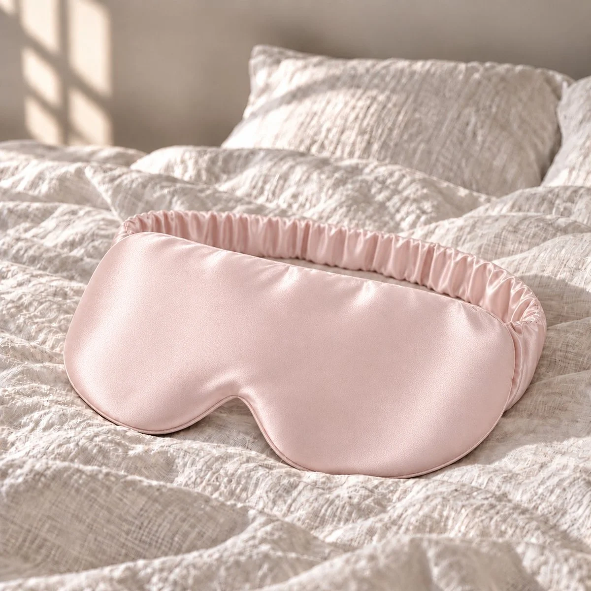 Masque de nuit en soie rose poudré posé sur un lit