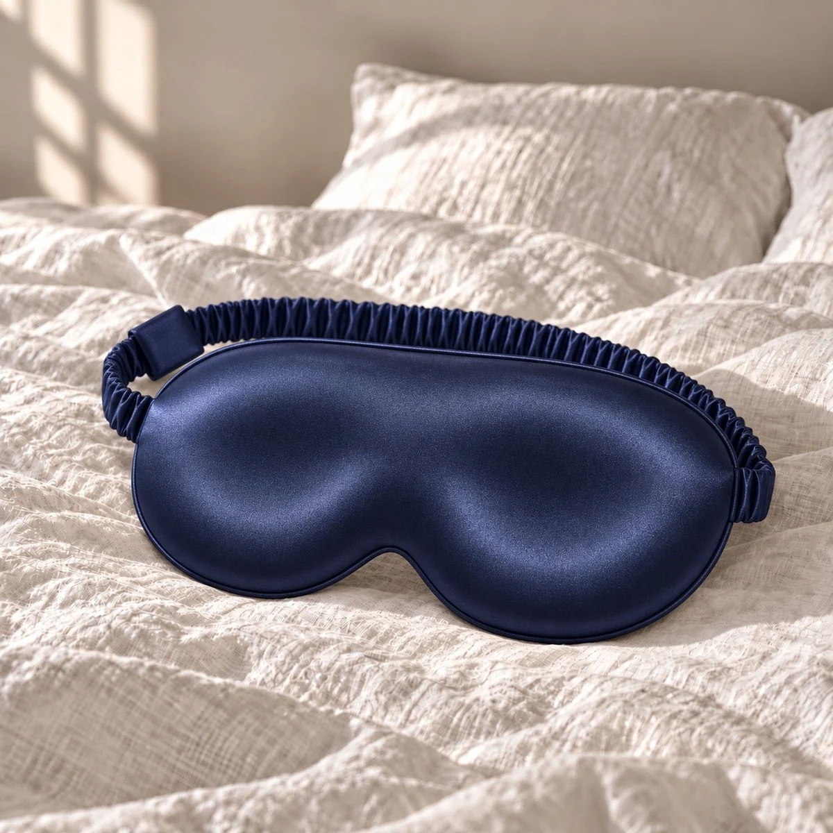 Masque de sommeil 3D en soie bleu nuit posé sur un lit