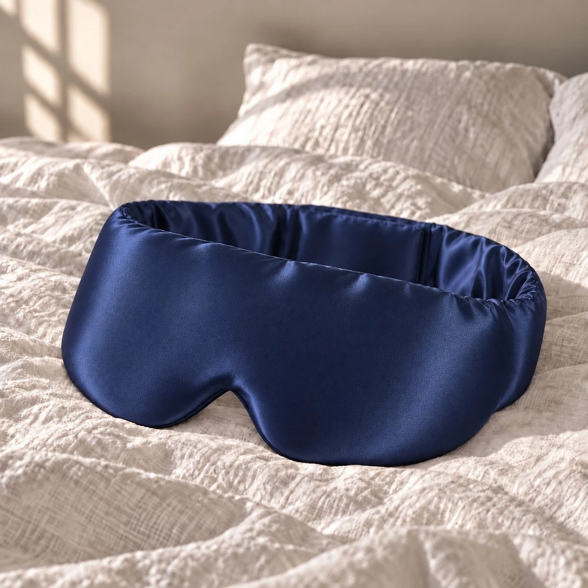 Masque de sommeil King en soie bleu nuit posé sur un lit